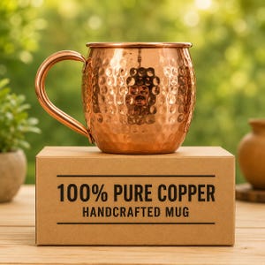 May include: A hammered copper mug with a curved handle sits atop a brown cardboard box. The box features black text that reads 100% PURE COPPER HANDCRAFTED MUG, framed by two horizontal black lines above and below the printed text.