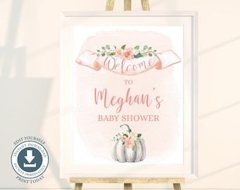May include: A white framed sign on a wooden easel featuring a watercolour peach background, a floral banner with the text Welcome to Meghan's Baby Shower, and a white pumpkin decorated with pink flowers and green leaves at the bottom of the print.