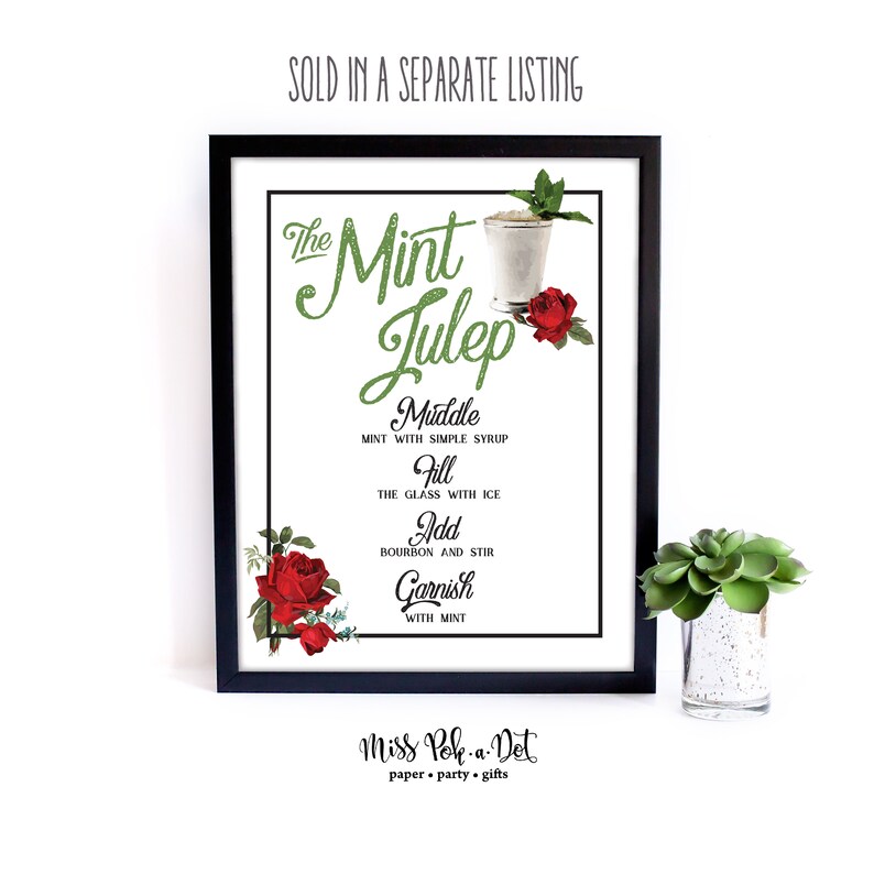 May include: A framed print with a black border, displaying a Mint Julep recipe. The title is in green glitter, with instructions below. Red roses and a small succulent in a decorative pot are also visible.