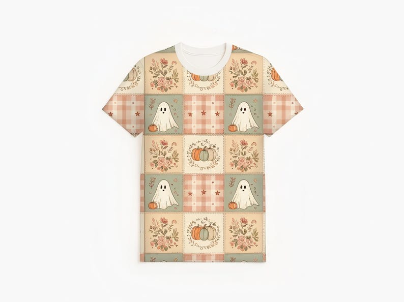 May include: A short-sleeve t-shirt featuring a repeating patchwork pattern of muted autumn colors. The design includes squares with white ghosts holding orange pumpkins, floral arrangements, and plaid squares with small stars in soft peach and sage green.