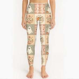 May include: Leggings featuring a patchwork-style grid pattern in muted tones of beige, sage green, and soft orange. The design includes repeating illustrations of white ghosts, orange pumpkins, and floral bouquets, interspersed with plaid squares.