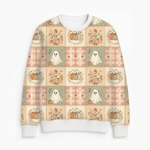May include: A long-sleeve crewneck sweatshirt featuring a repeating patchwork pattern. The design includes alternating squares of white ghosts with orange pumpkins, floral arrangements, and a soft peach and white plaid with small star accents.