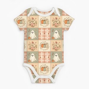 May include: A short-sleeved baby bodysuit featuring a patchwork pattern of alternating squares. The design includes illustrations of white ghosts, orange and blue pumpkins, floral arrangements, and small stars on a soft plaid background.