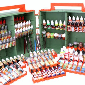 May include: An olive green and bright orange modular storage case featuring multiple interior shelves and exterior racks filled with numerous small plastic dropper bottles of various paint colors and several thin paintbrushes stored upright.