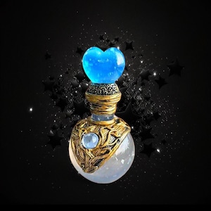 May include: A decorative glass bottle with a spherical base and a bright blue heart-shaped stopper. The neck features textured gold metalwork with a leaf-like pattern and a small, round, light blue stone embedded in the center of the gold casing.
