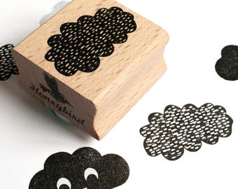 Pode incluir: Um carimbo de madeira com um desenho de nuvem preto e branco. O carimbo está sobre uma superfície branca com vários outros carimbos de nuvem preto e branco.