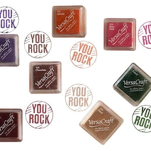 K&ouml;nnte beinhalten: Sortiment von zehn Stempelkissen in verschiedenen Farben, jedes mit dem Text "VersaCraft" und "You Rock" auf dem Kissen. Die Stempelkissen sind quadratisch und rechteckig.