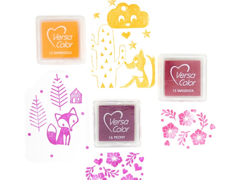 Pode incluir: Um conjunto de tr&ecirc;s almofadas de tinta para carimbar, com uma almofada amarela etiquetada "Versa Color 12 Marigold", uma almofada magenta etiquetada "Versa Color 15 Magenta" e uma almofada roxa etiquetada "Versa Color 16 Peony".