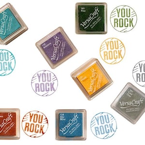 K&ouml;nnte beinhalten: Sortiment von zehn Stempelkissen in verschiedenen Farben, jedes mit dem Text "VersaCraft" und "You Rock" auf dem Kissen bedruckt. Die Stempelkissen sind in einem Kreis auf wei&szlig;em Hintergrund angeordnet.