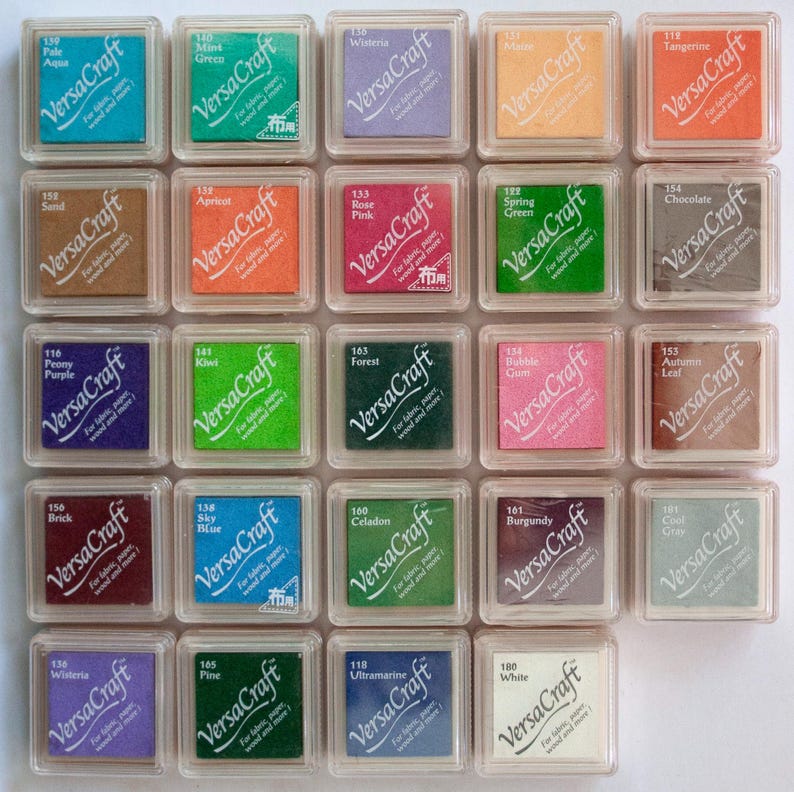 K&ouml;nnte beinhalten: Eine Sammlung von 20 Stempelkissen in verschiedenen Farben, jede mit dem Markennamen "VersaCraft" und einem Farbnamen beschriftet. Die Stempelkissen sind in einem Rastermuster auf einer wei&szlig;en Oberfl&auml;che angeordnet.