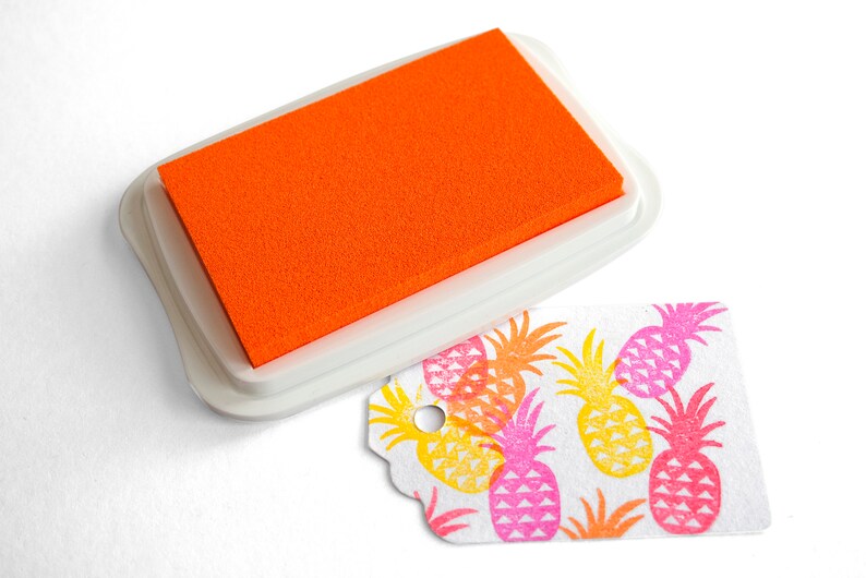 Pu&ograve; includere: Tavoletta d'inchiostro arancione con una custodia in plastica bianca e un'etichetta bianca con un motivo a ananas stampato in rosa, giallo e arancione.