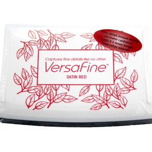 Puede incluir: Una almohadilla de tinta blanca con una etiqueta roja que dice "Captures fine details like no other VersaFine Satin Red". La etiqueta tiene un dise&ntilde;o floral rojo alrededor de los bordes.