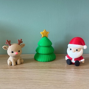 Könnte beinhalten: Ein Set aus drei kleinen Figuren, bestehend aus einem beigen Rentier mit rosa Nase, einem grünen Weihnachtsbaum mit goldenem Stern an der Spitze und einer Weihnachtsmannfigur mit roter Mütze und weißem Bart, alle mit strukturierter Oberfläche.