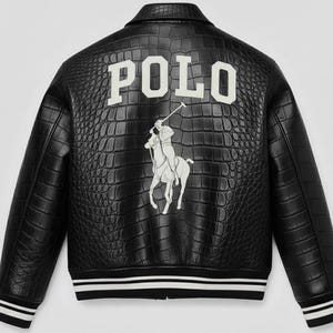 May include: A black jacket with a textured crocodile-embossed pattern. The back features the white text POLO above a large white graphic of a person riding a horse while holding a mallet. The jacket has black and white striped ribbed cuffs and hem.