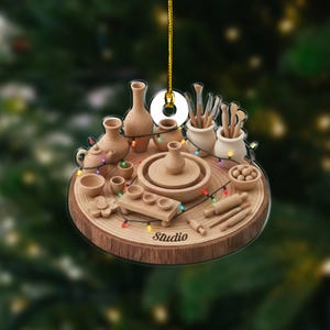May include: A circular hanging ornament featuring a miniature pottery studio scene on a wood slice base. It includes clay pots, vases, tools, and a wheel, decorated with a string of colorful lights. The word Studio is printed on the base.