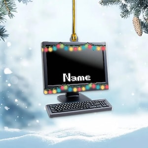 May include: A computer monitor and keyboard ornament hanging from a gold string. The monitor screen is black with the word Name in white pixelated text, framed by a string of colorful Christmas lights along the top and bottom edges.