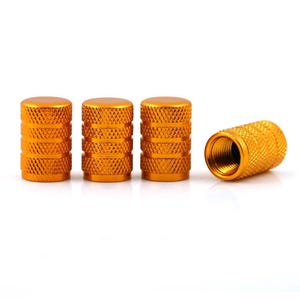 May include: Four cylindrical valve stem caps with a bright gold finish. Each cap features a textured diamond-patterned knurled grip along the exterior surface. One cap is positioned on its side, revealing the internal metal threading for attachment.