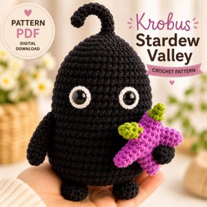 May include: A black crocheted Krobus figure from Stardew Valley with large white-rimmed eyes and a small curled antenna, holding a purple star-shaped item with green accents. The image includes text reading Pattern PDF Digital Download.