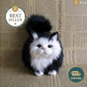 May include: A plush toy cat with long, fluffy black and white fur. The cat has a white face, chest, and paws, with black fur on its ears, back, and tail. It features dark, round eyes and a small pink nose, standing in a seated position.