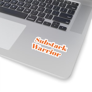 May include: A rectangular sticker with a white border featuring the orange text Substack Warrior in a bold, sans-serif font. The sticker is applied to the silver surface of a laptop, positioned below the keyboard and to the right of the trackpad.