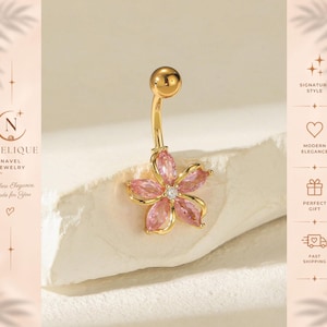 May include: A gold-toned navel ring featuring a flower-shaped charm with five marquise-cut pink gemstones arranged around a central clear round stone. The curved barbell has a smooth gold ball at the top end, providing a polished metallic finish.