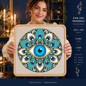 May include: A square wooden embroidery hoop containing a cross stitch pattern of a blue, white, and gold evil eye mandala. The text reads EVIL EYE MANDALA, 200 x 200 stitches, 6 DMC colors, 3 PDF files, and finished sizes for 14ct, 16ct, and 18ct fabric.