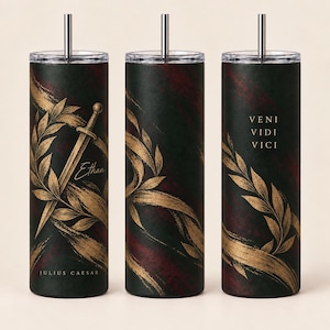 May include: Three cylindrical tumblers with lids and straws featuring a dark green and maroon textured background, gold laurel leaf illustrations, a sword, and the text Ethan, Julius Caesar, and Veni Vidi Vici in a gold serif font.