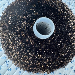 Peut inclure: Une tête de brosse circulaire et dense dotée de poils rigides brun foncé disposés en motif radial autour d'un noyau cylindrique central en plastique blanc translucide. Les poils sont courts, de longueur uniforme et forment une surface texturée.