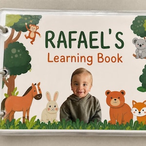 May include: A rectangular learning book bound with three white plastic rings. The cover features the text RAFAEL'S Learning Book, a central photograph of a child, and illustrations of a monkey, koala, horse, rabbit, bear, and fox in a forest.