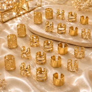 Op de afbeelding: Een verzameling goudkleurige metalen ringen en oorklemmen in diverse ontwerpen, waaronder gladde banden, gedraaide touwtexturen en ingewikkelde filigraanpatronen. Deze kleine, open cirkelvormige accessoires zijn gerangschikt op een lichtgekleurde ondergrond.