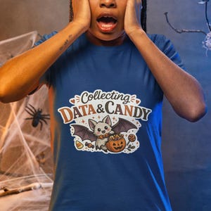 Puede incluir: Una camiseta azul de manga corta con el gráfico de un murciélago de dibujos animados sosteniendo un cubo de calabaza lleno de dulces. El texto sobre el murciélago dice "Collecting DATA & CANDY" en una fuente estilizada, rodeado de estrellas.