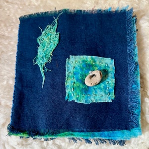 Puede incluir: Un peque&ntilde;o diario de tela azul con un borde deshilachado. La portada tiene un parche cuadrado de tela azul y verde con una peque&ntilde;a piedra blanca en el centro. Hay un parche m&aacute;s peque&ntilde;o de tela azul y verde en la esquina superior izquierda.