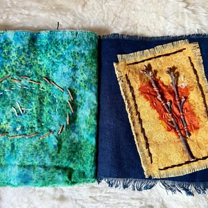 Puede incluir: Un libro hecho a mano con dos p&aacute;ginas. La p&aacute;gina izquierda es de tela azul y verde con un c&iacute;rculo marr&oacute;n cosido alrededor del borde. La p&aacute;gina derecha es de tela azul oscuro con un cuadrado de tela amarillo en el centro. El cuadrado de tela amarillo tiene un dise&ntilde;o de ramitas marrones y un peque&ntilde;o trozo de tela naranja en el centro.