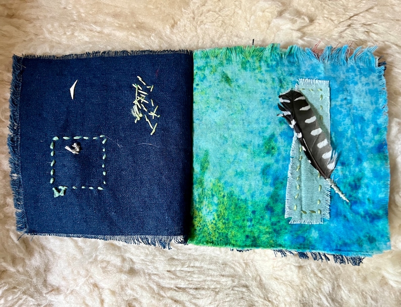 Puede incluir: Un diario de tela hecho a mano con una cubierta de mezclilla azul y una cubierta de te&ntilde;ido anudado verde y azul. La cubierta de mezclilla tiene un peque&ntilde;o cuadrado cosido con hilo blanco y una pluma est&aacute; unida a la cubierta de te&ntilde;ido anudado.