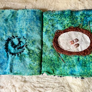Puede incluir: Un libro de tela hecho a mano con una cubierta de m&aacute;rmol azul y verde. El libro est&aacute; abierto para revelar una p&aacute;gina con un nido marr&oacute;n y tres perlas rosadas en su interior.