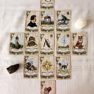 Może przedstawiać: Zestaw trzynastu kart wyroczni Lenormand ułożonych w kształt krzyża, przedstawiających ilustracje pierścienia, mężczyzny, ogrodu, ryby, wieży, myszy, biczów, kosy, lisa, ptaków, słońca, psa i trumny, wraz z białą świecą oraz ciemnym kamieniem.