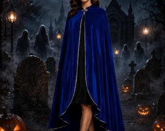 May include: A floor-length royal blue velvet cloak featuring a silver metallic trim along the edges and a decorative silver clasp at the neckline. The garment is worn over a simple black dress and paired with black ankle boots.