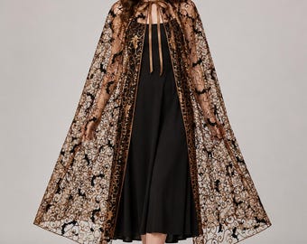 May include: A floor-length hooded cape made of sheer black and gold lace featuring a repeating bat pattern. The cape is fastened at the neck with a thin brown ribbon tie and is worn over a simple black sleeveless dress with a square neckline.