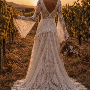 May include: A floor-length white lace dress featuring long bell sleeves, a deep V-neckline, and a fitted bodice that transitions into a flowing skirt with a train. The intricate lace pattern covers the entire garment, including the flared sleeves.