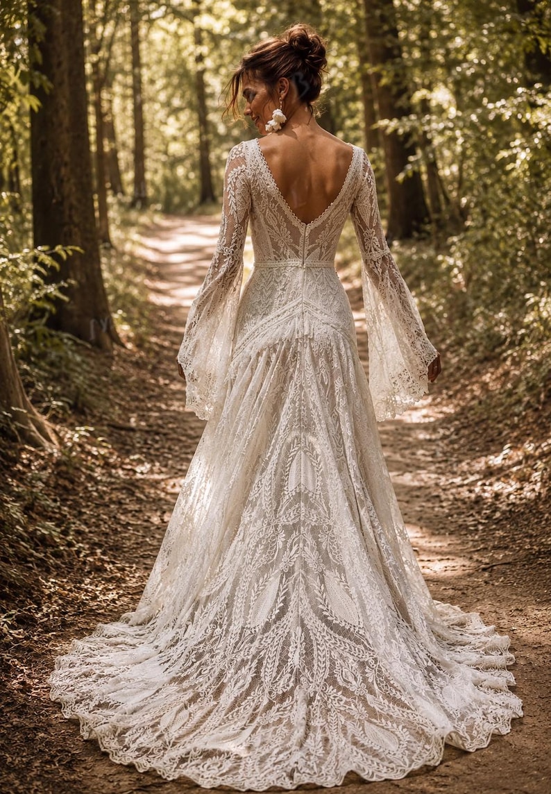 May include: A floor-length ivory lace gown featuring long bell sleeves, a deep V-shaped back, and a fitted bodice that transitions into a flowing skirt with a train. The intricate lace pattern covers the entire garment, highlighting the detailed floral and leaf motifs throughout the fabric design.