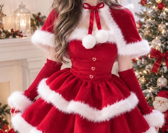 May include: A red dress with white faux fur trim, featuring a tiered skirt, a matching capelet with two white pom-poms, and a red ribbon tie. The bodice includes three small heart-shaped buttons, and the outfit is paired with long red sleeves.