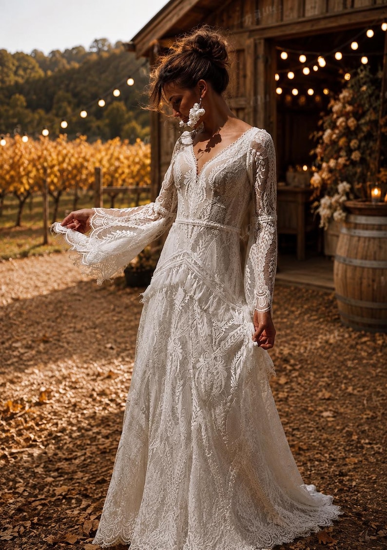 May include: A floor-length white lace dress featuring long, flared sleeves, a deep V-neckline, and intricate floral embroidery throughout. The garment includes a fitted bodice with a defined waistline and a flowing skirt with layered lace detailing.
