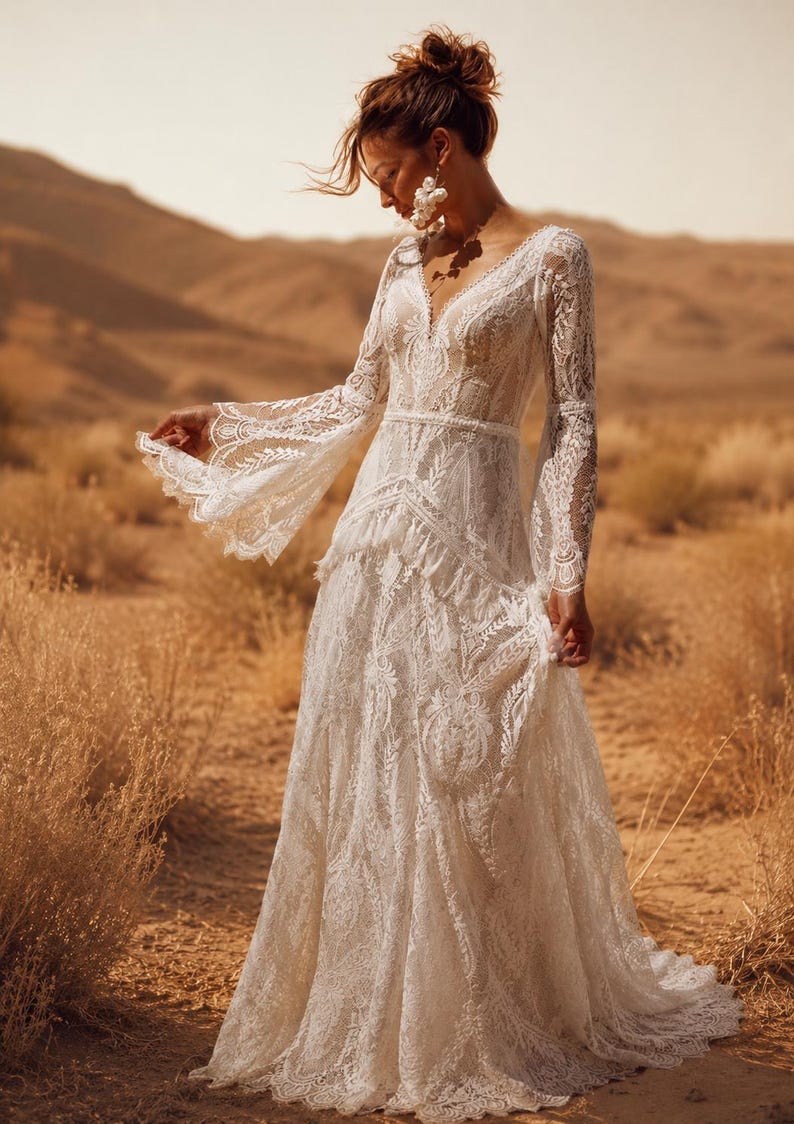 May include: A floor-length white lace dress featuring long bell sleeves, a V-neckline, and a fitted bodice with a layered skirt. The intricate floral lace pattern covers the entire garment, which includes a defined waistline and flared cuffs.
