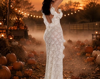 May include: A floor-length white lace dress featuring a deep open back, ruffled shoulder straps, and a ruffled hemline. The garment is constructed from a delicate floral lace fabric that extends from the bodice down to the floor-length skirt.
