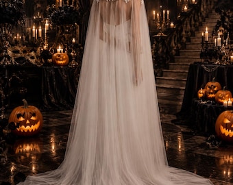 May include: A floor-length white bridal cape featuring a high neck with intricate lace detailing at the shoulders and upper back. The garment is crafted from sheer, flowing tulle fabric that extends into a long, sweeping train behind the wearer.