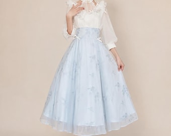 May include: A two-piece dress featuring a white sheer long-sleeve blouse with a high collar, ruffled accents, and a light blue midi skirt with a floral pattern, a high waist, and two small white bows at the front waistline.