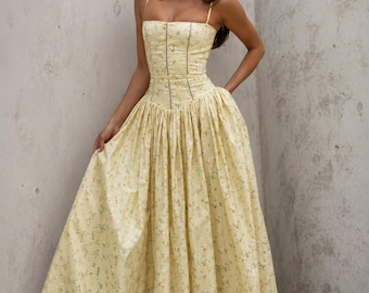 May include: A floor-length yellow dress featuring a small blue and white floral pattern, a corset-style bodice with thin spaghetti straps, a defined waistline, and a full, pleated skirt that extends to the floor with a structured silhouette.