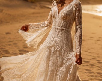 May include: A floor-length ivory lace dress featuring long, flared sleeves, a deep V-neckline, and a fitted bodice that transitions into a flowing, tiered skirt with intricate floral patterns and scalloped edges throughout the entire garment.