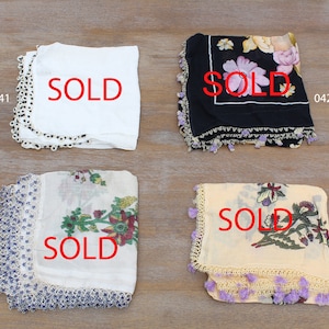 May include: Four square scarves with floral patterns and lace trim. The scarves are white, black, cream, and beige. Each scarf has the word "SOLD" printed in red.