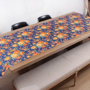 May include: A wooden table with a blue and orange floral tablecloth. The table is set with two black chairs and a beige bench.